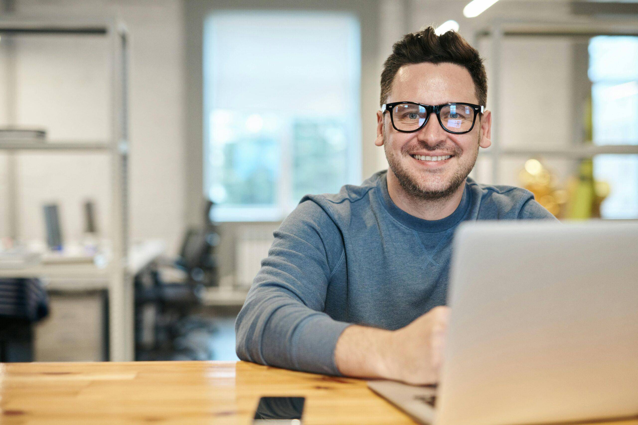 Happy man wearing glasses working remotely on laptop in modern office environment. pexels-photo-3184611-3184611